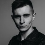 Stylish black and white studio portrait of a young caucasian man in a contemplative pose.